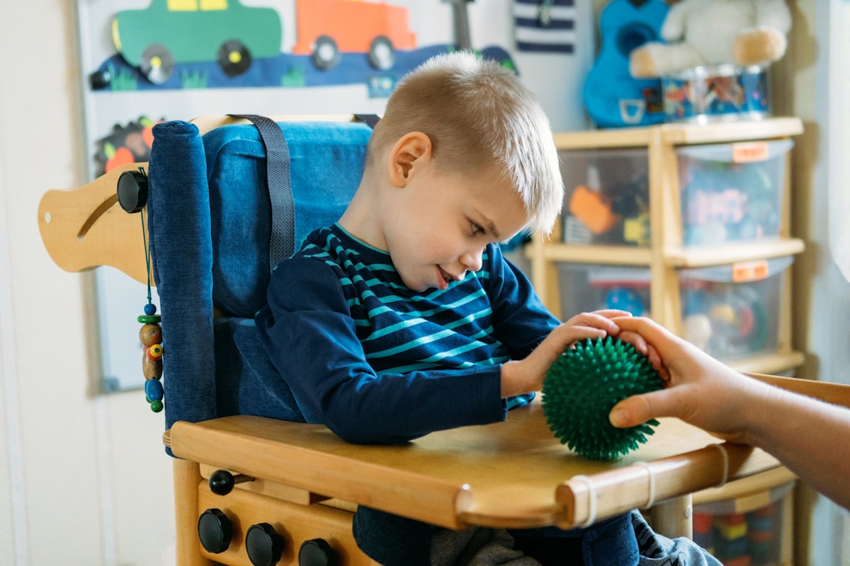 Boy with with Cerebral Palsy in special chair play with mom at home